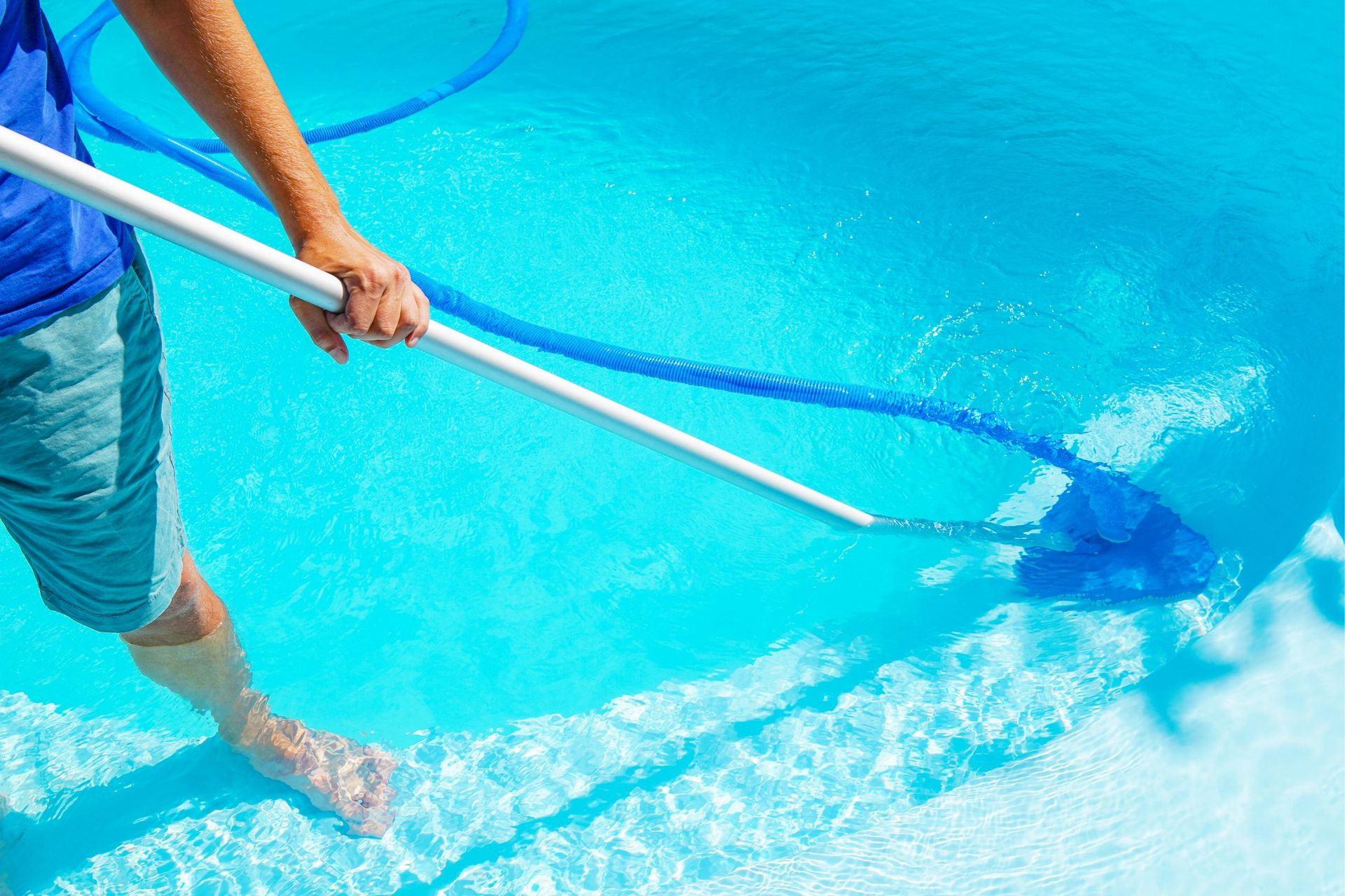 Person using a net to scoop debris from a bright blue swimming pool.
