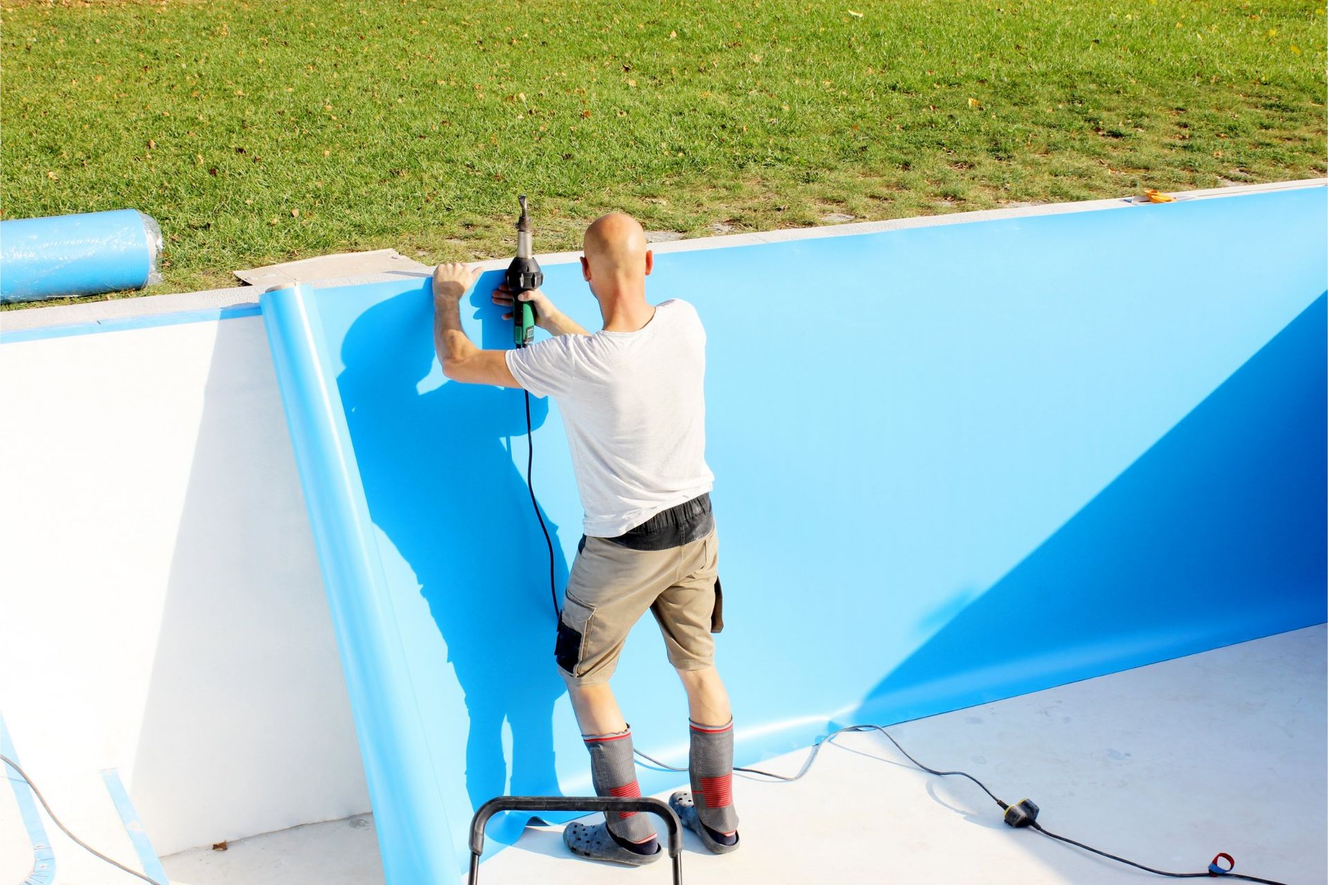 Man installing blue pool liner in a partially built pool, outdoors.