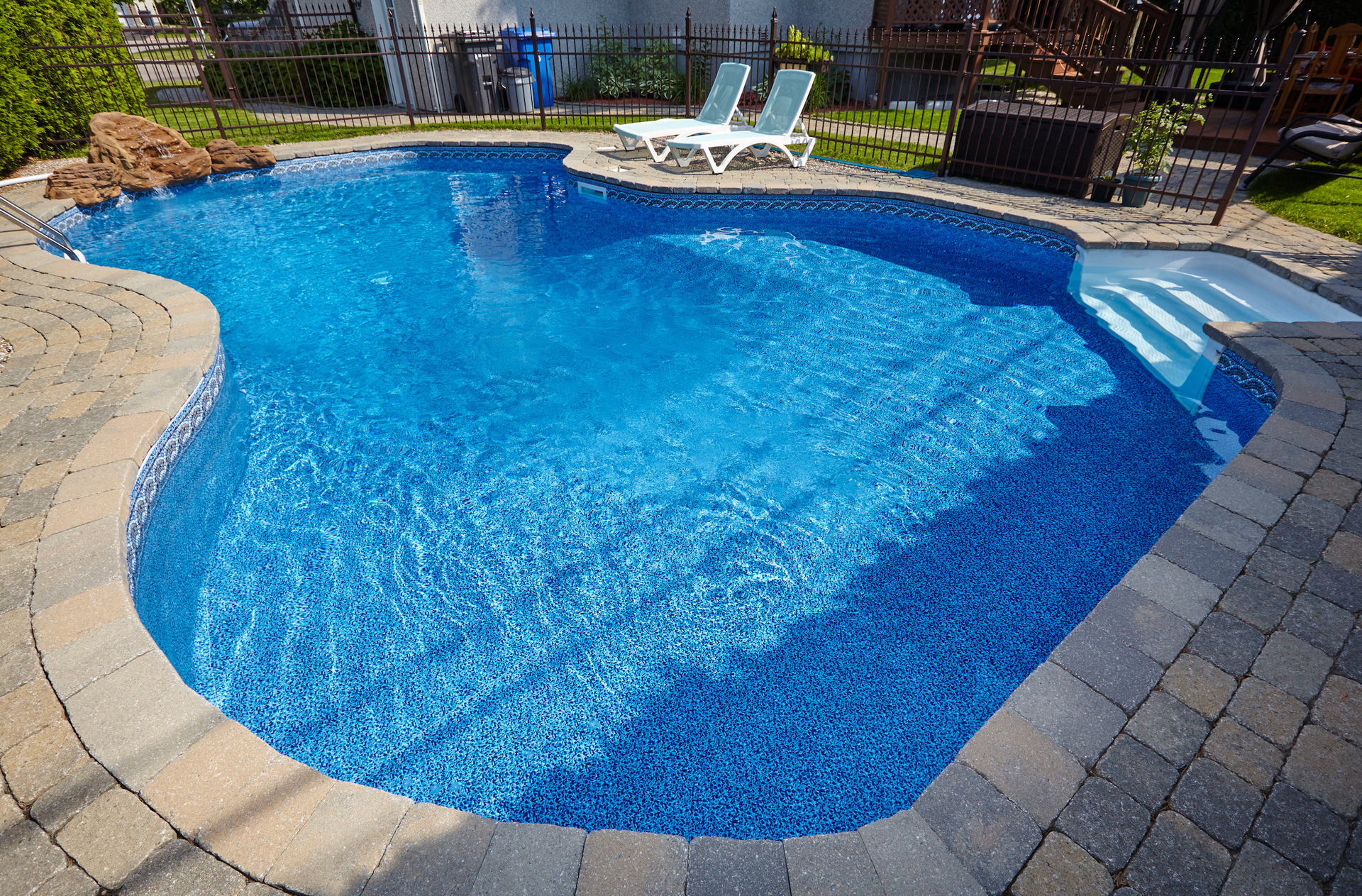 Swimming pool with blue water and stone deck. Two lounge chairs sit nearby.