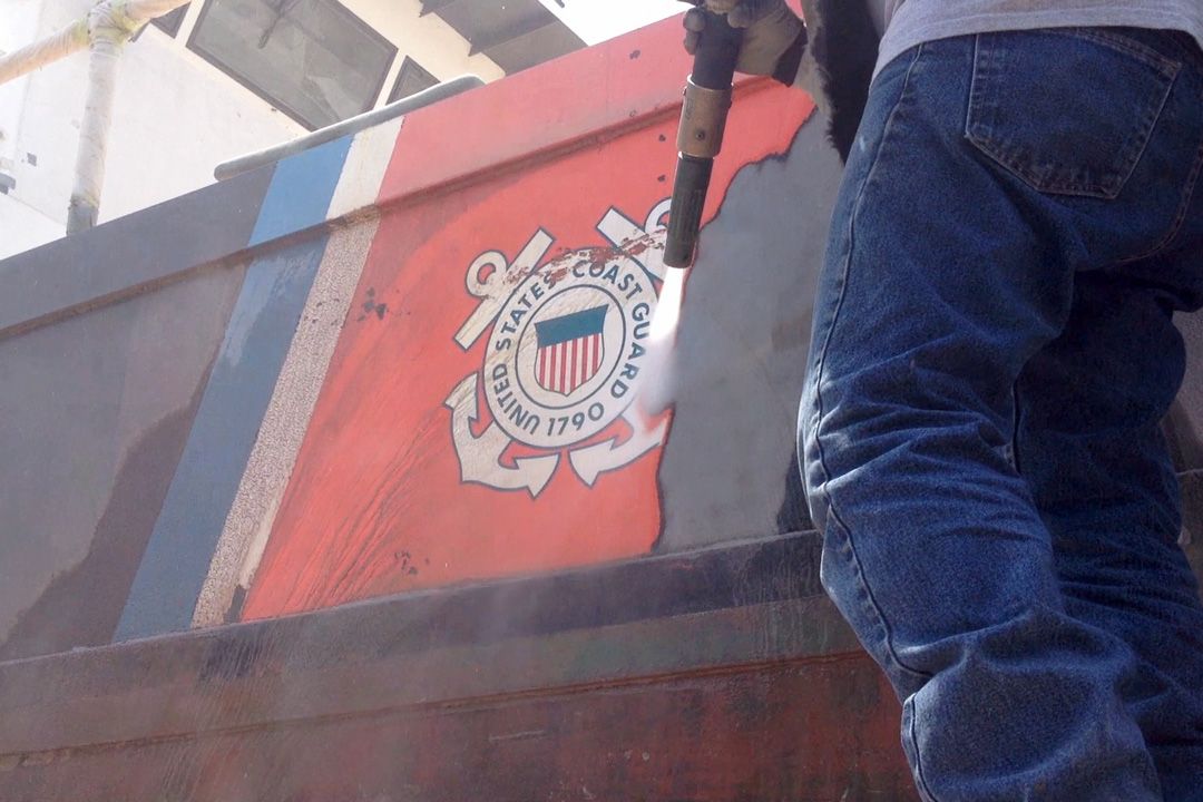 A man in a white suit is painting a boat.