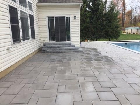 Grey paver patio outside a house with a pool in the background.