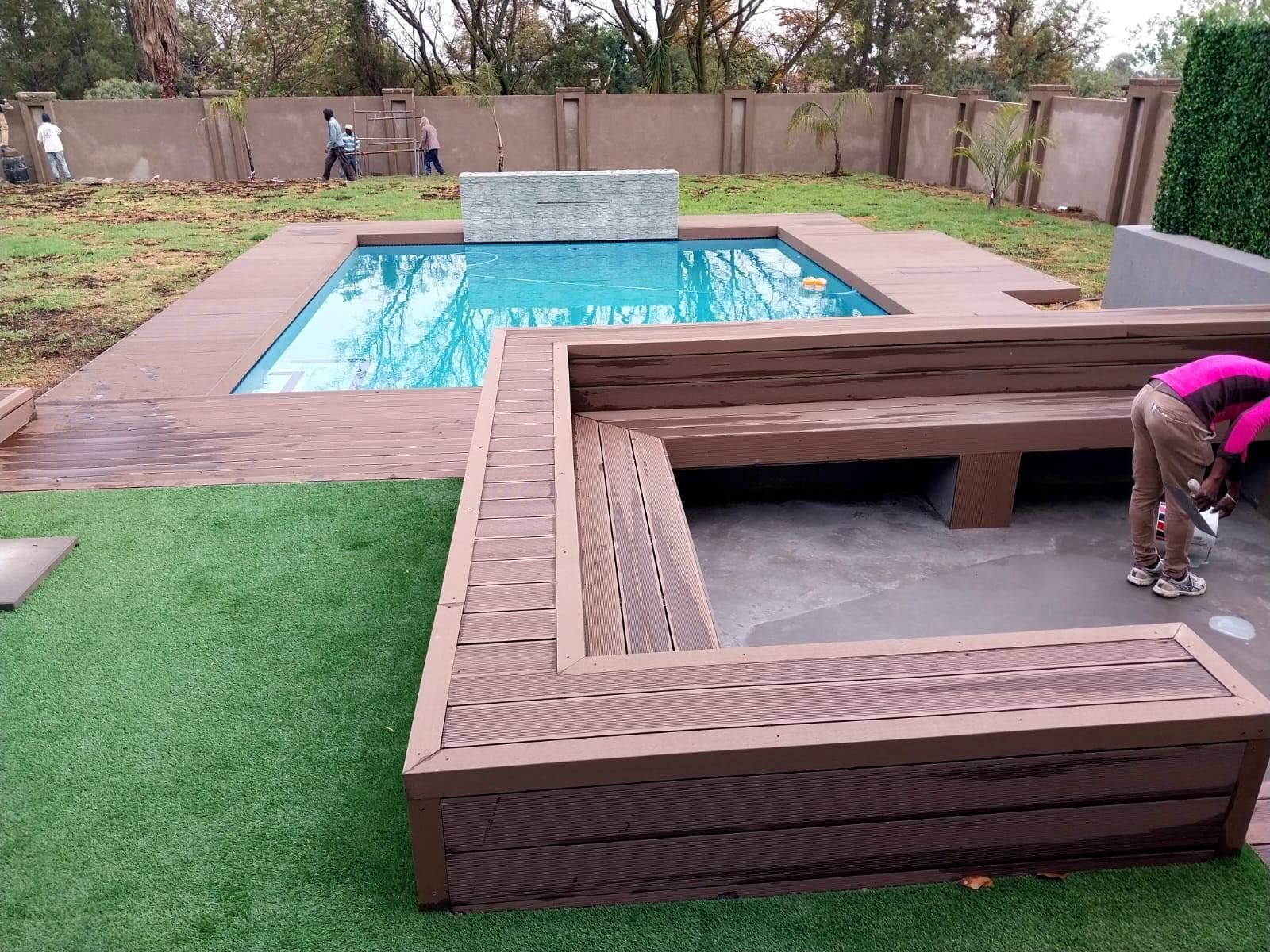 Rectangular swimming pool filled with blue water, with a vacuum hose inside; surrounded by brown deck.