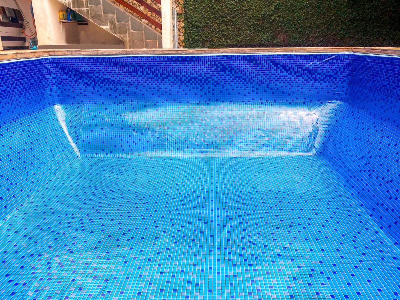 Empty blue tiled swimming pool with steps.