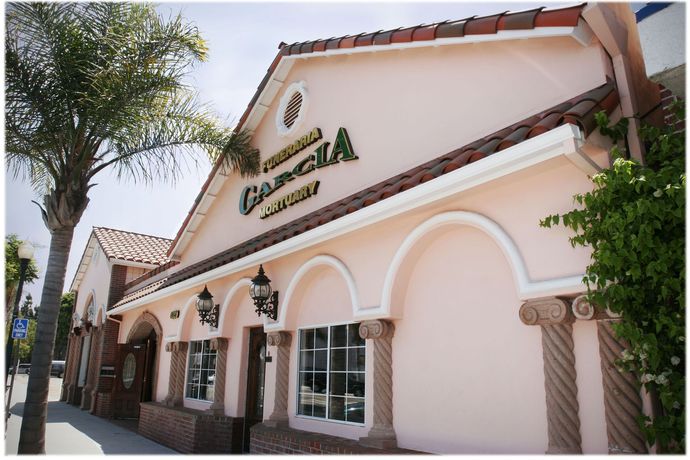 Exterior of a white stucco building with arched windows, a red tile roof, and palm trees.