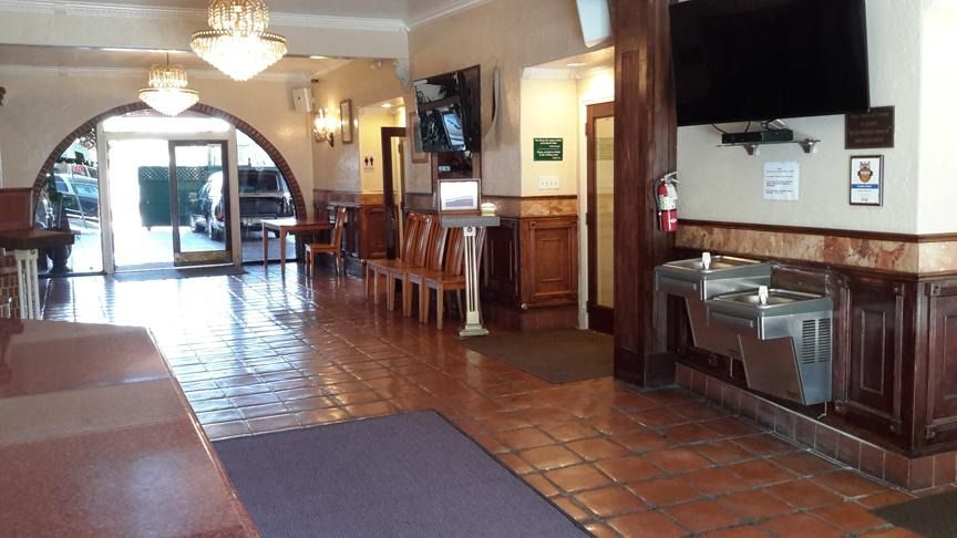 Lobby with terracotta tile floor, wooden benches, chandelier, reception desk, and arched doorway to a bright entrance.