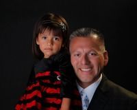 Smiling man in a suit holding a child in a red-and-black striped sweater against a black background