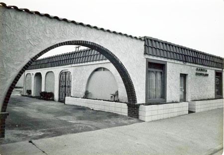 Black-and-white photo of a small stucco building with arched entrance and tiled roof