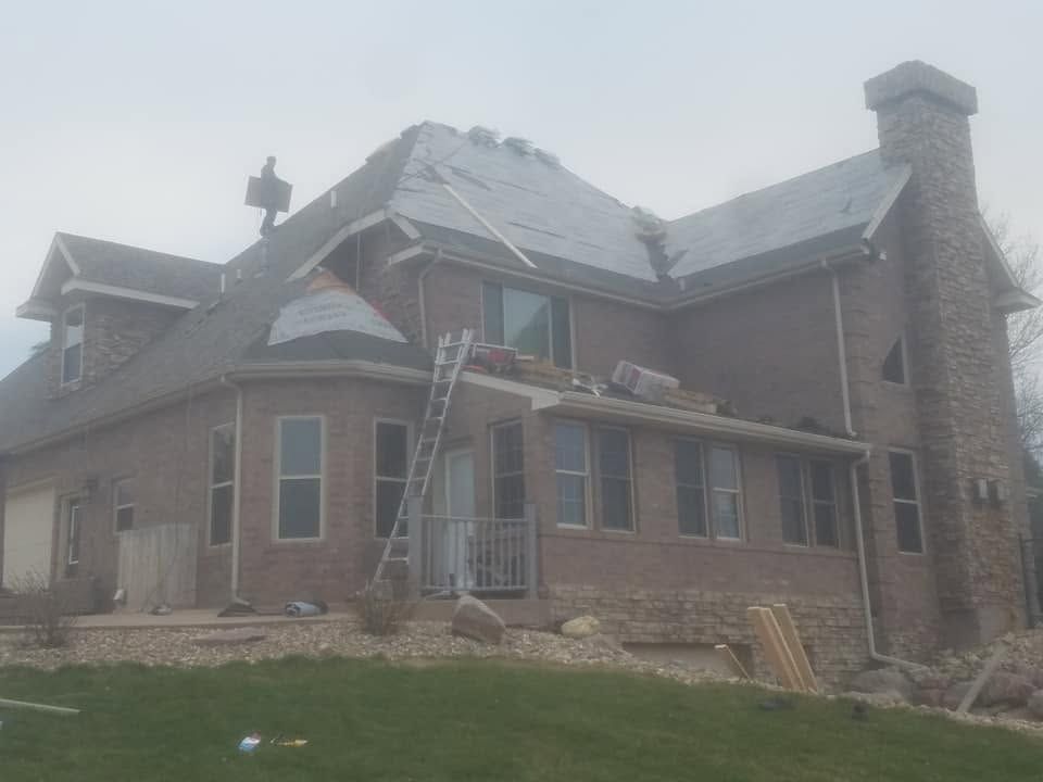 Large brick house with a snowy roof and stone foundation under construction