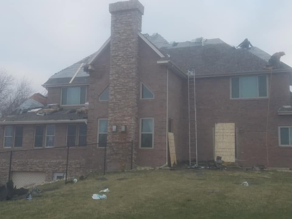 Brick house exterior with chimney, boarded door, and a grassy yard under a gray sky