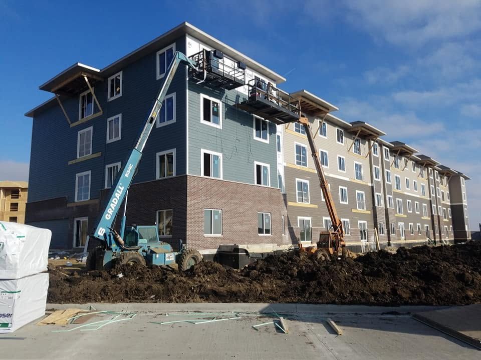 Apartment building under construction with two boom lifts against a clear blue sky