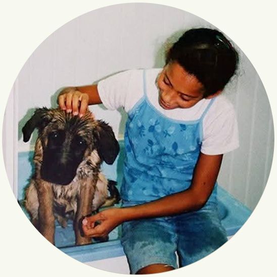 Meisje aait een natte hond; beiden glimlachen. Blauw hemdje, wit shirt, lichtblauwe achtergrond.