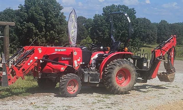 Red tractor with front loader and backhoe parked on a gravel lot under a blue sky