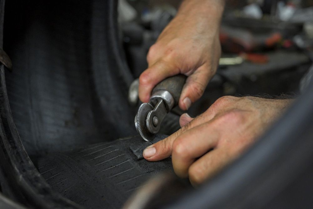 Hands using pliers to repair a tire or rubber surface in a workshop
