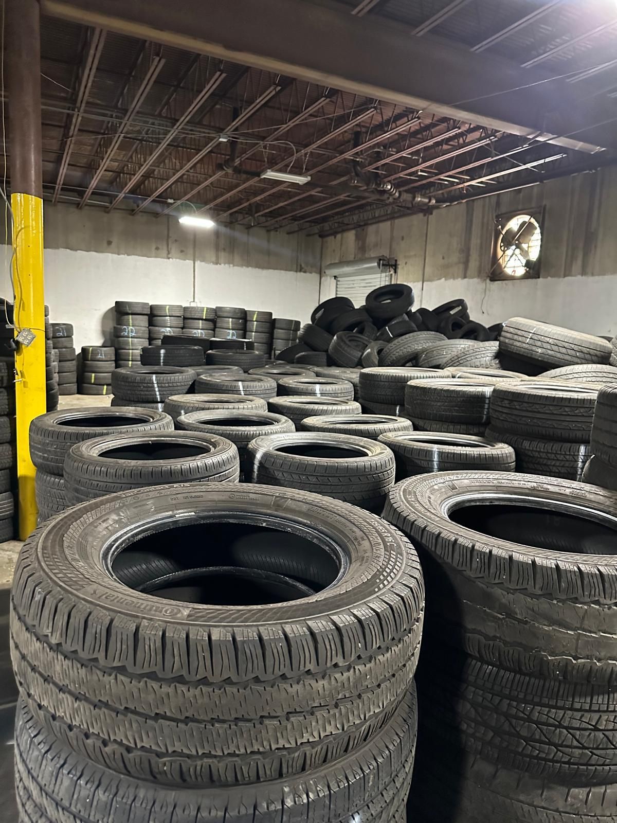 Stacked used tires stored in a warehouse, with tires piled across the floor and against the back wall.