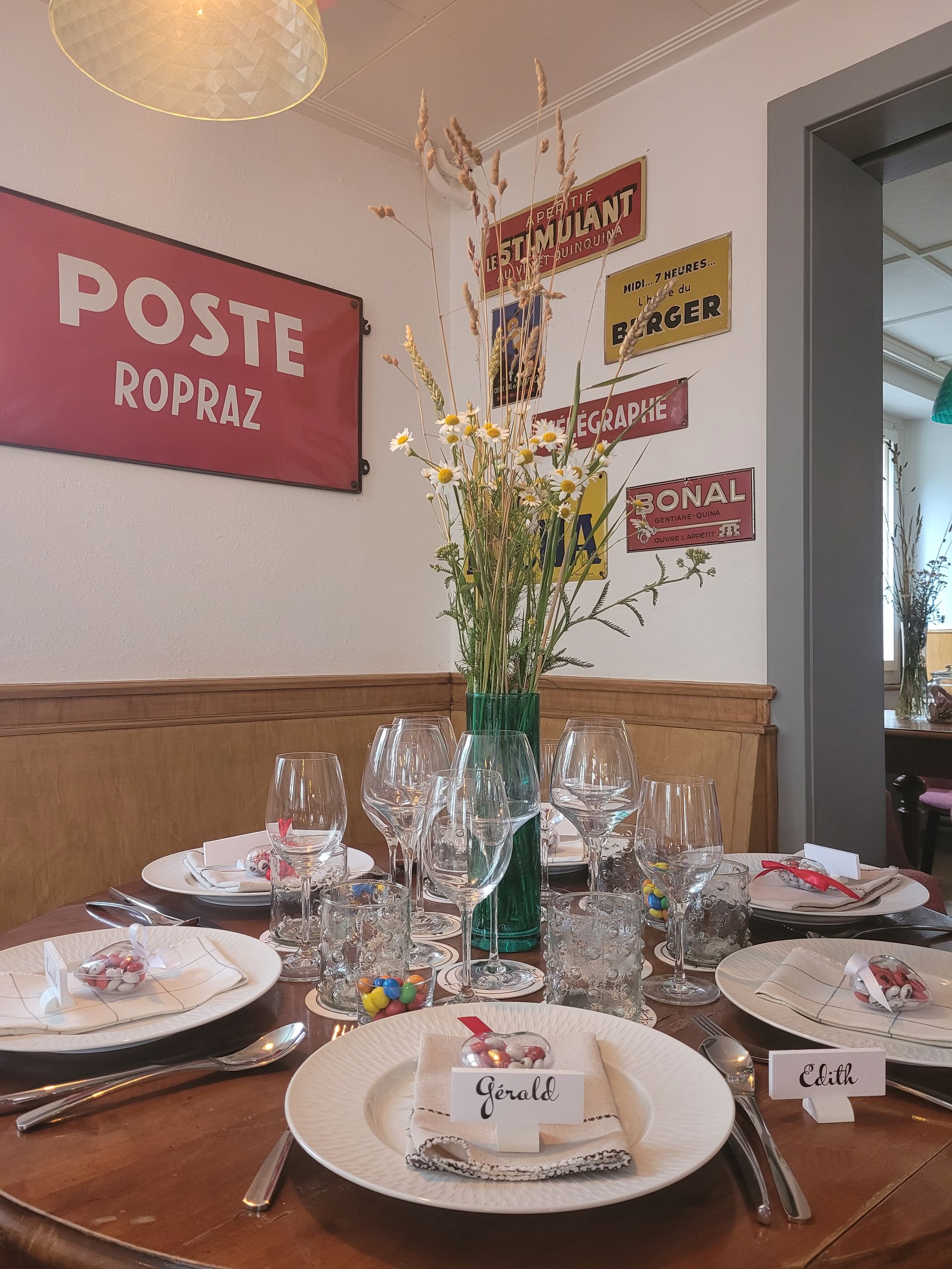 Table dressée avec des fleurs, des verres et des marque-places, dans une pièce ornée d'enseignes vintage.