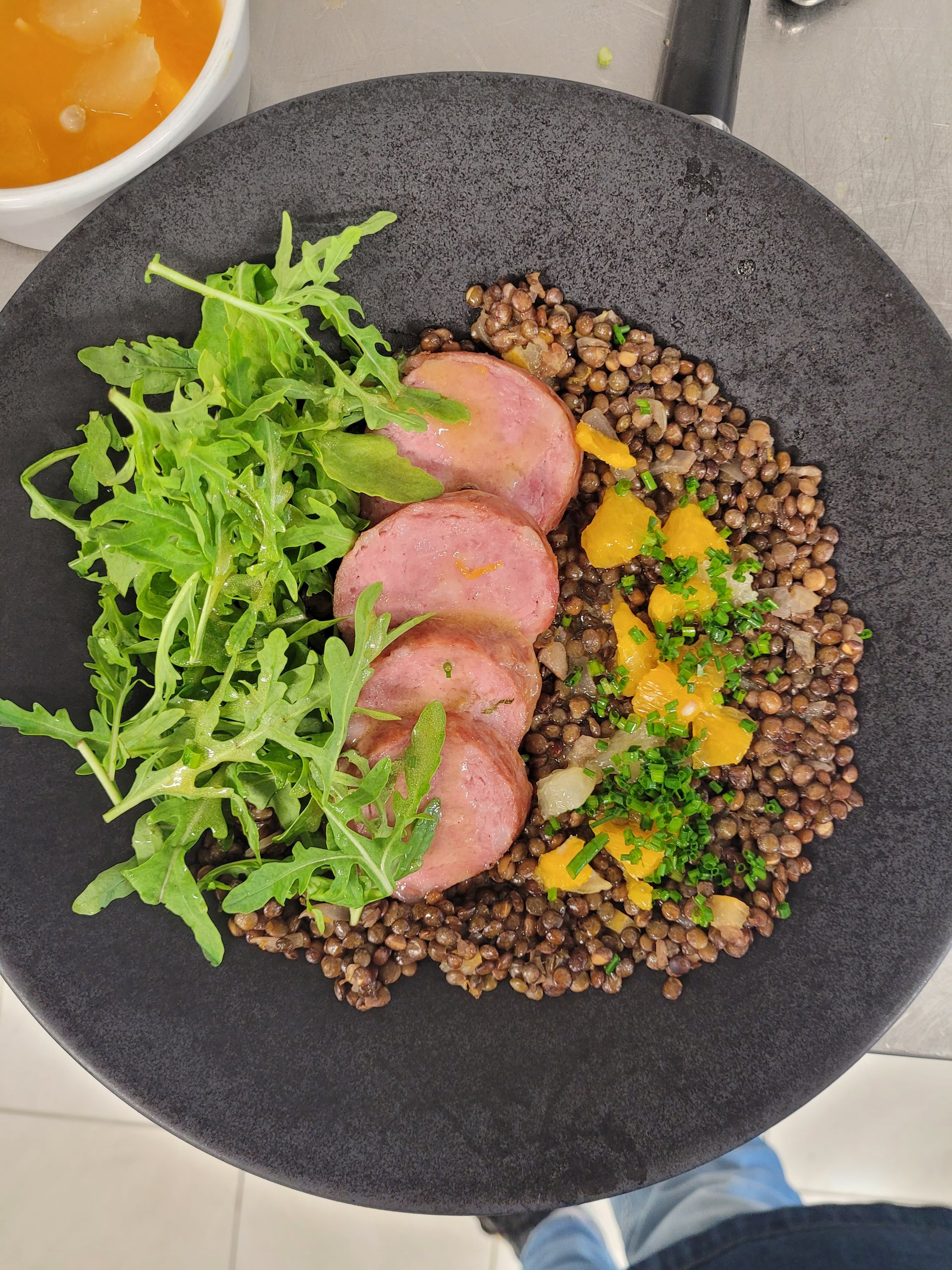 Assiette : saucisse tranchée, lentilles, mangue, roquette et un bol de soupe.
