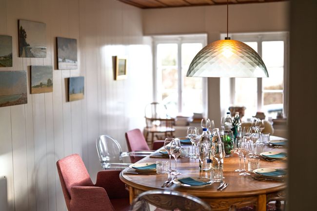 Salle à manger avec une longue table dressée pour un repas, chaises roses, fleurs, bougies et planches à découper décoratives.