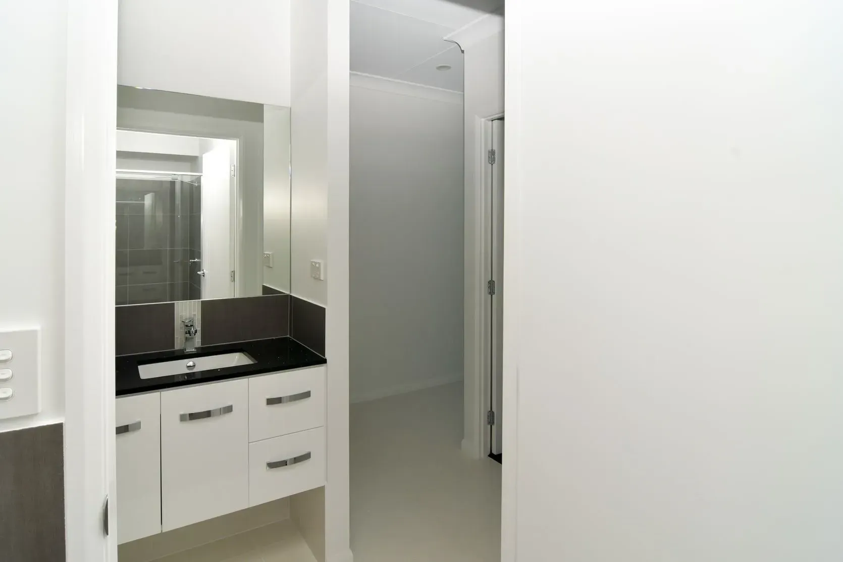Bathroom Interior With White Cabinets, Dark Countertop, Large Mirror, And Open Doorway — B & C Cabinets in Mareeba, QLD