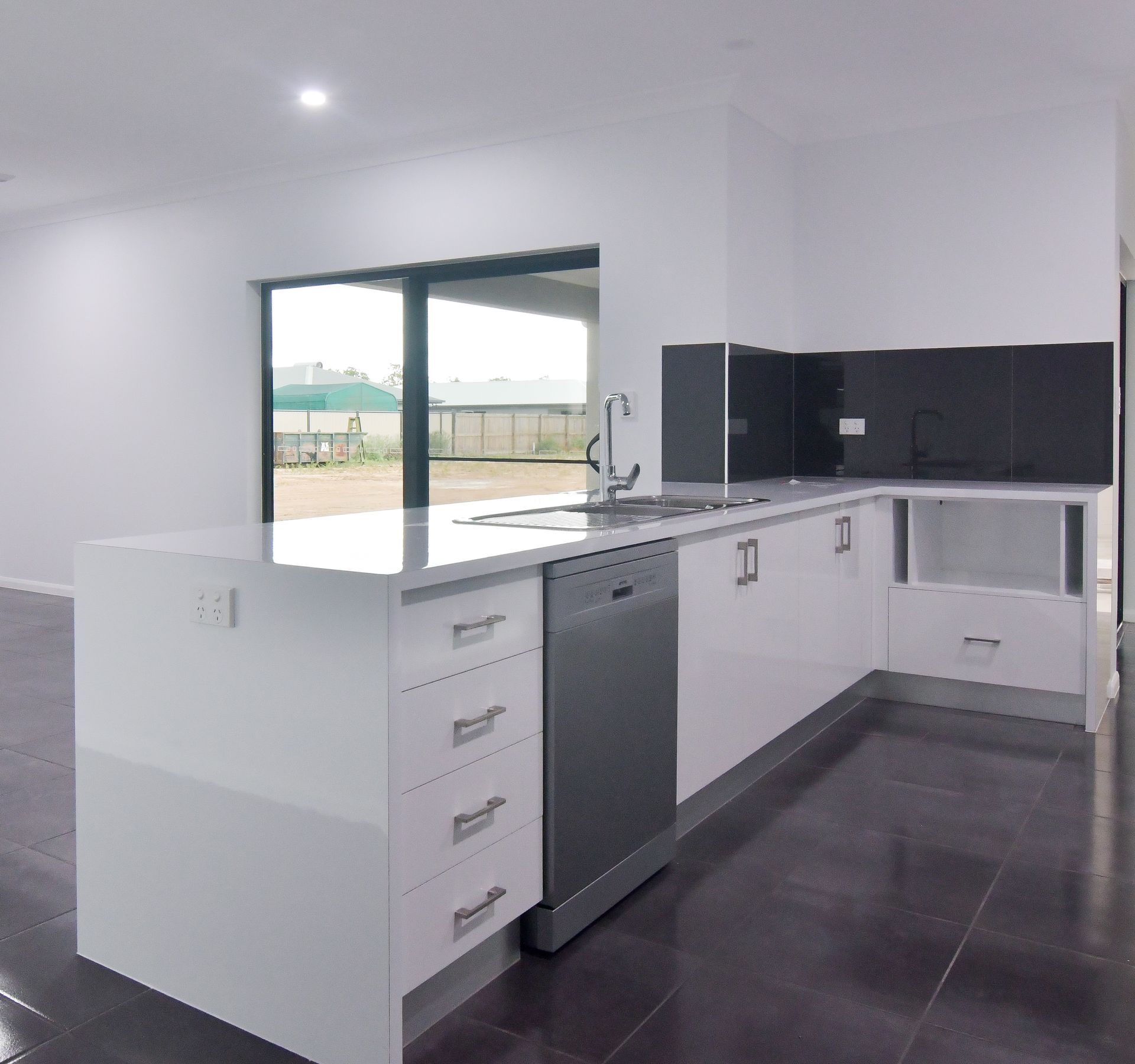 Modern White Kitchen With A Grey Tiled Floor. Stainless Steel Appliances And Black Backsplash — B & C Cabinets in Mareeba, QLD