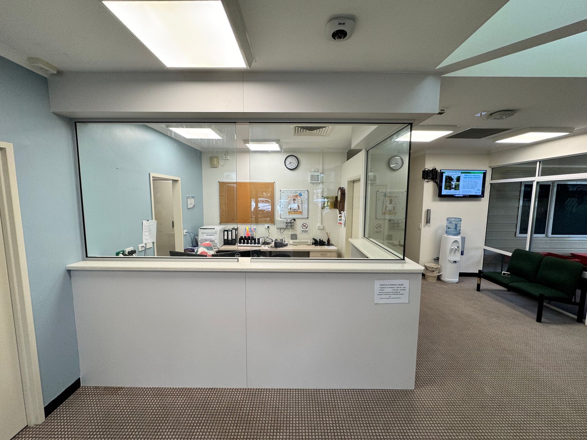 Reception Desk With Glass Barrier, Light Blue Wall, Waiting Area With Chairs And A Water Cooler — B & C Cabinets in Mareeba, QLD