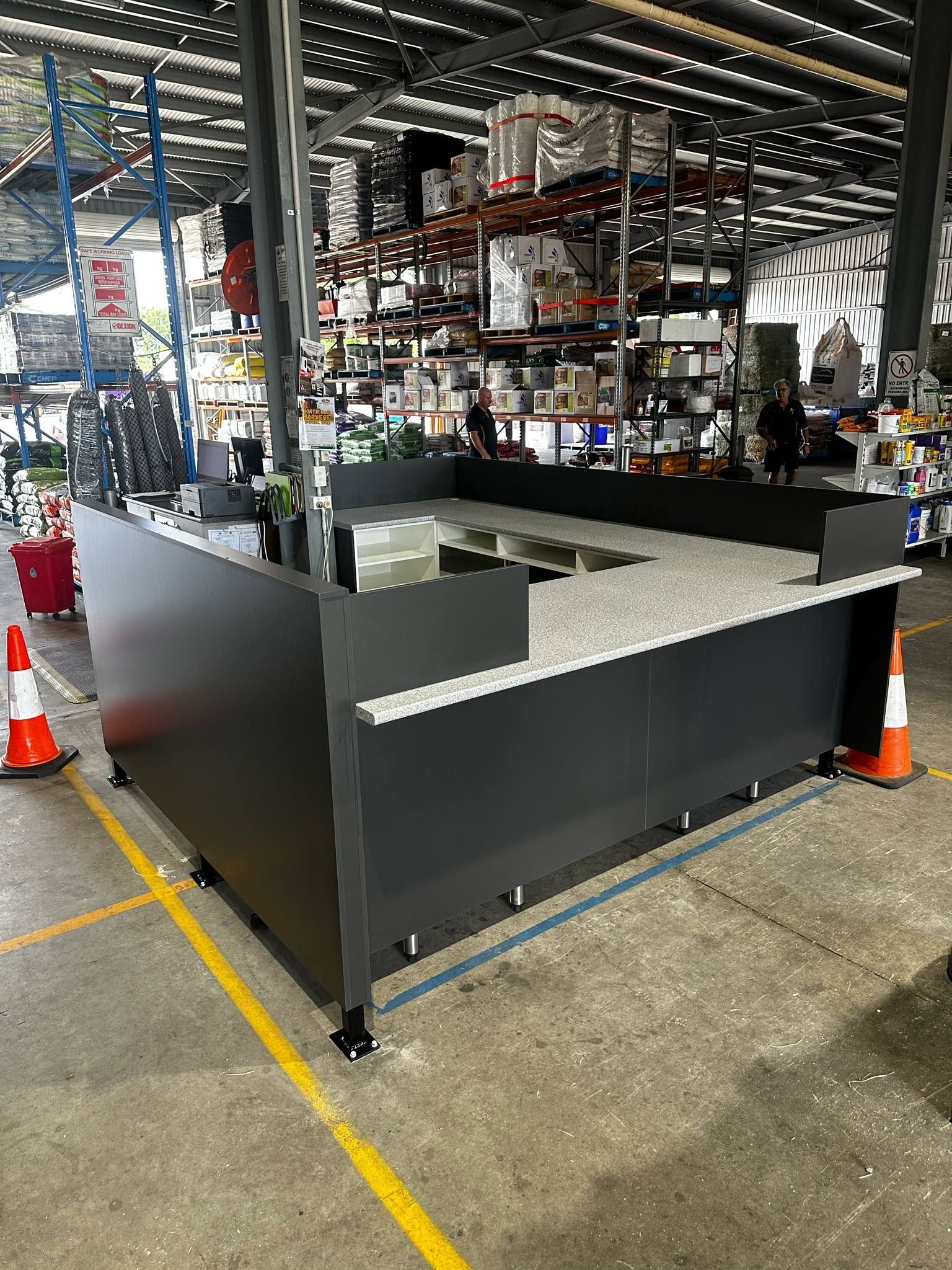 Dark Gray Rectangular Counter With Speckled Top, In Warehouse Setting With Shelving And Traffic Cones — B & C Cabinets in Mareeba, QLD
