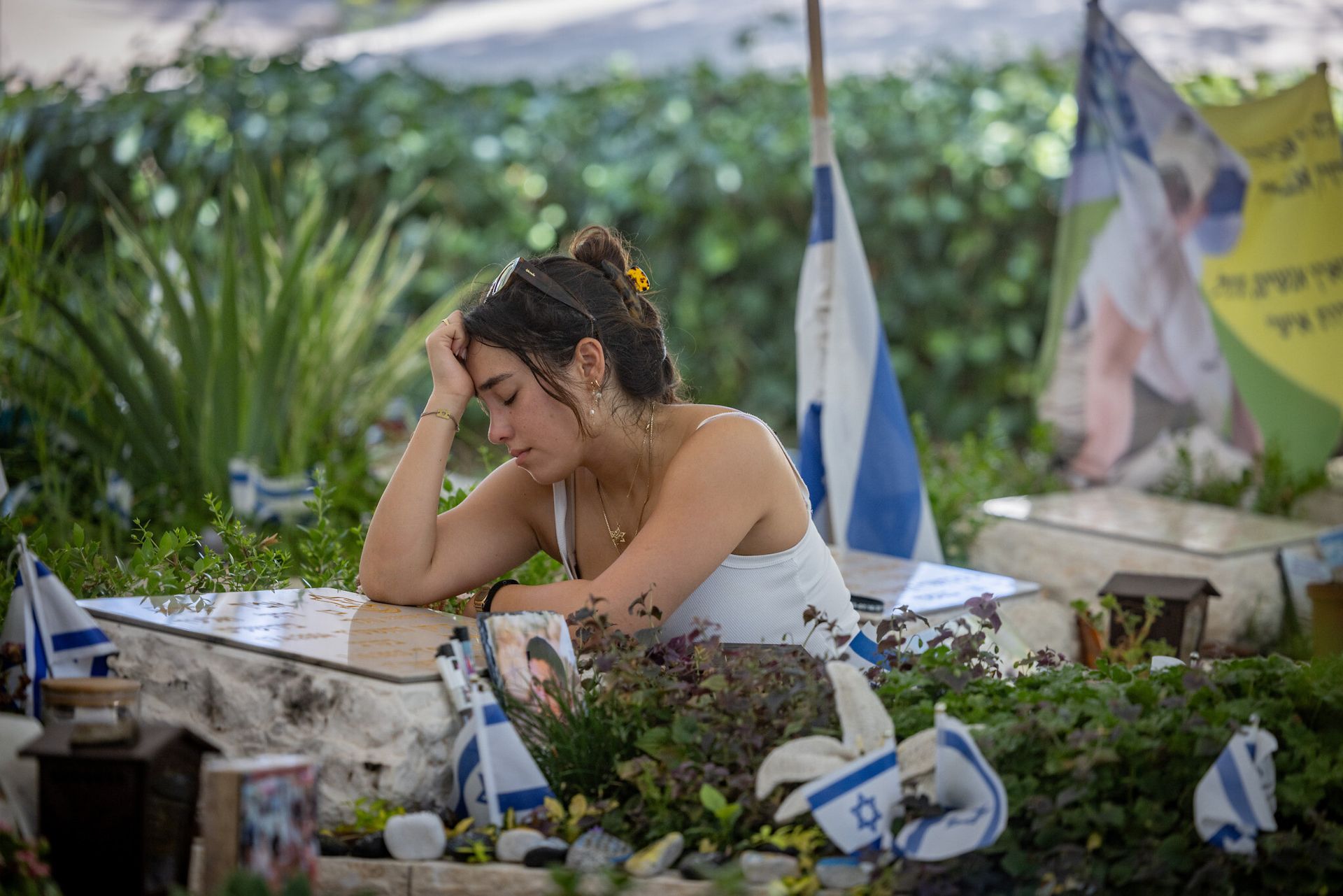 A woman is sitting in a cemetery with her head in her hands.