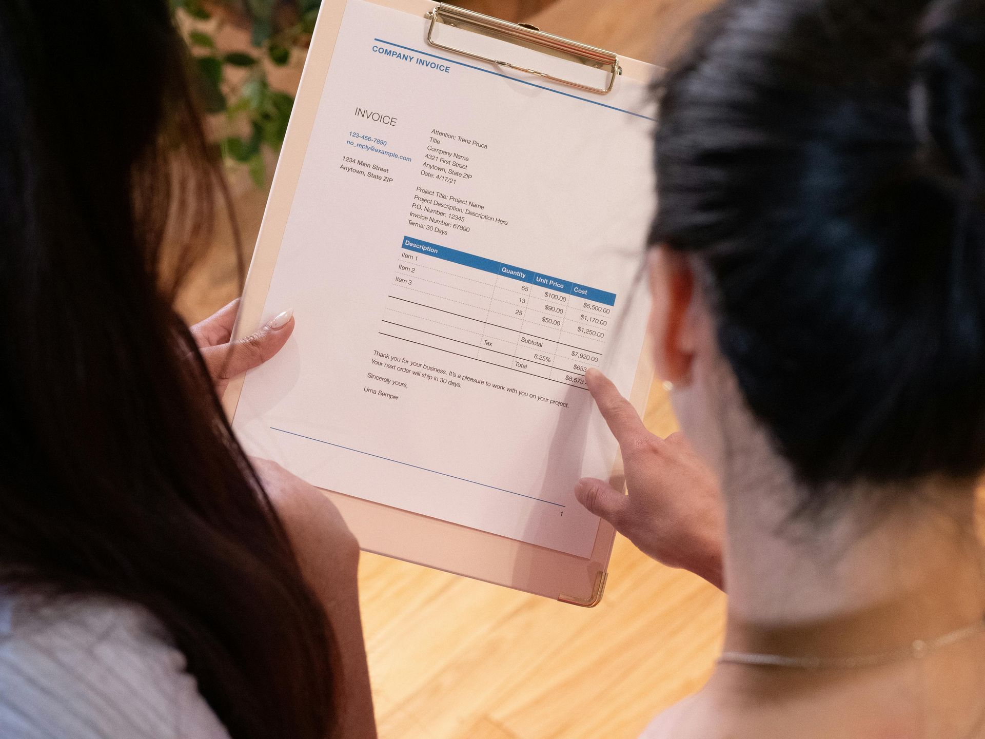 Two women are looking at an invoice on a clipboard.
