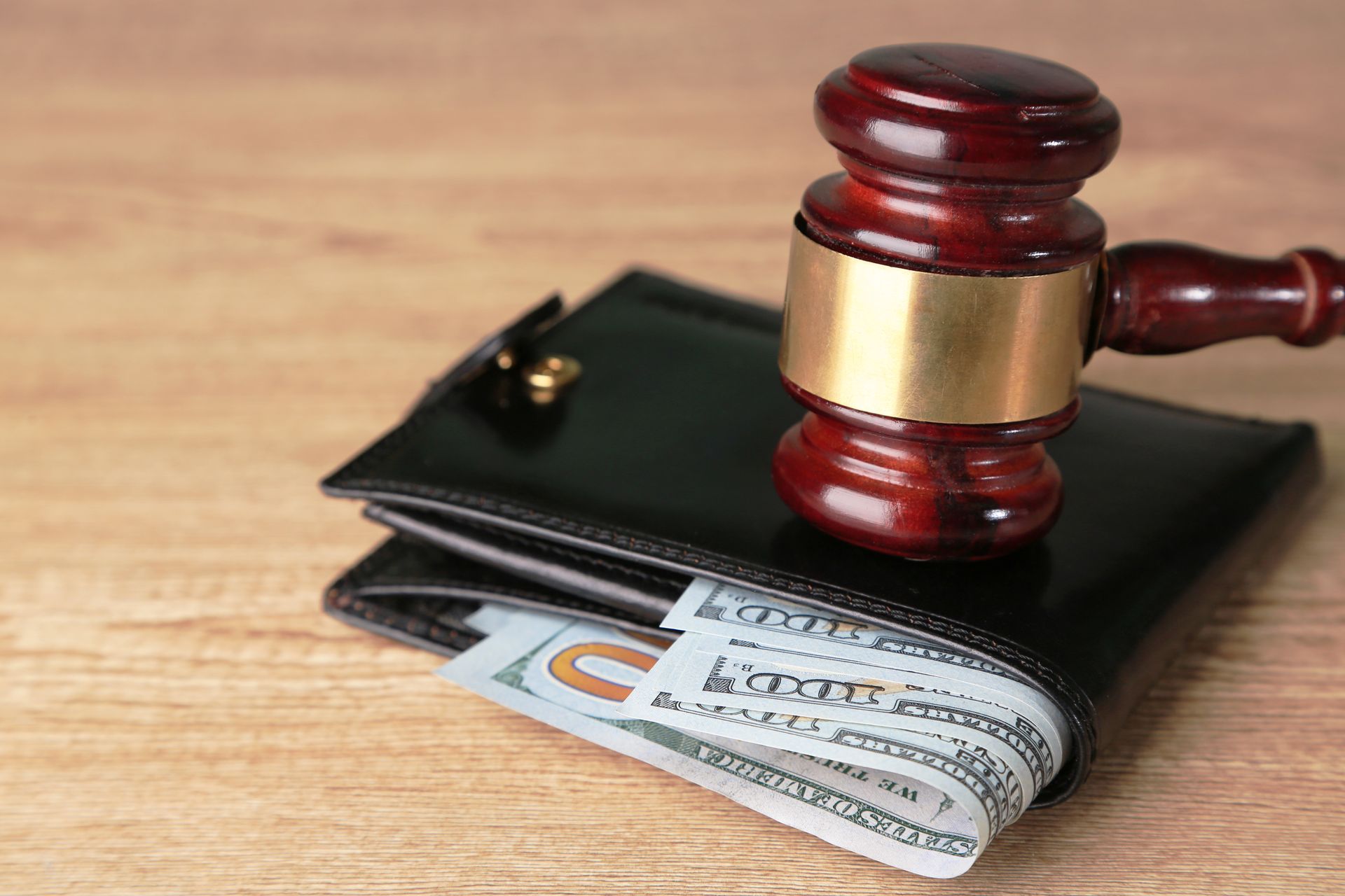 A wooden judge 's gavel is sitting on top of a black wallet.