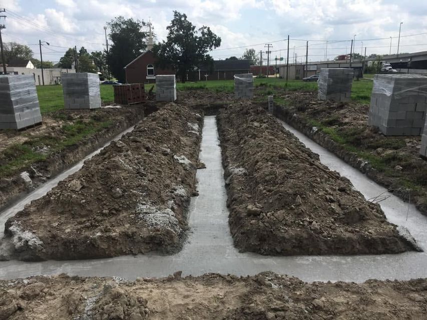 Rows of fresh soil and concrete foundations on a construction site under cloudy skies.