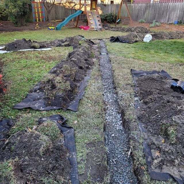 Backyard garden beds with black tarp edges and a gravel trench running down the center.