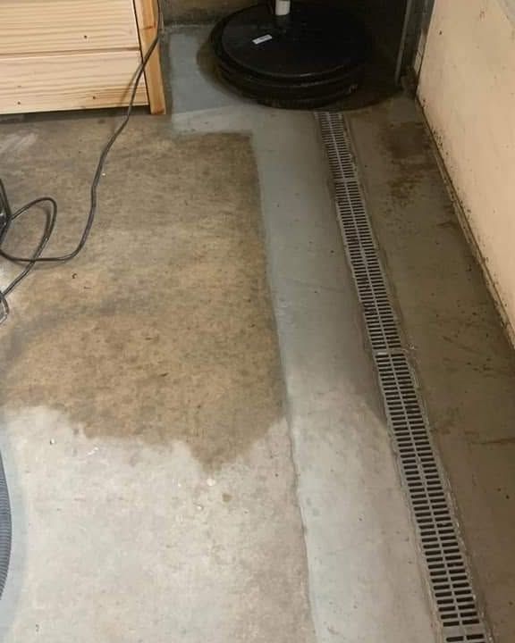 Concrete floor with wet patch and a long drain grate along the wall