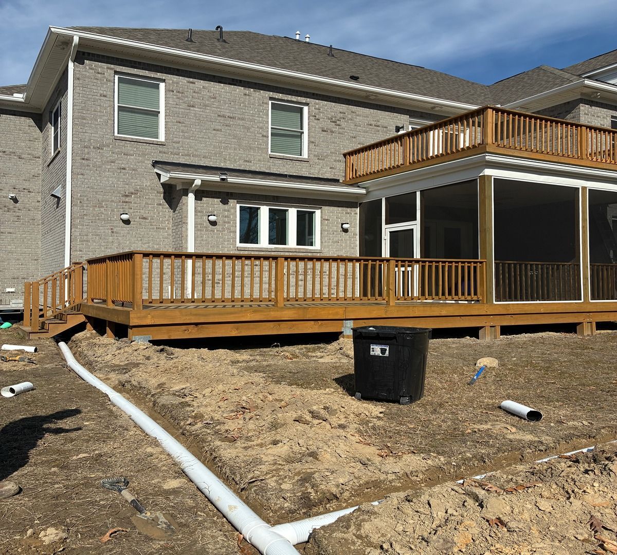 New house with gray siding and wooden decks under construction in a dirt yard