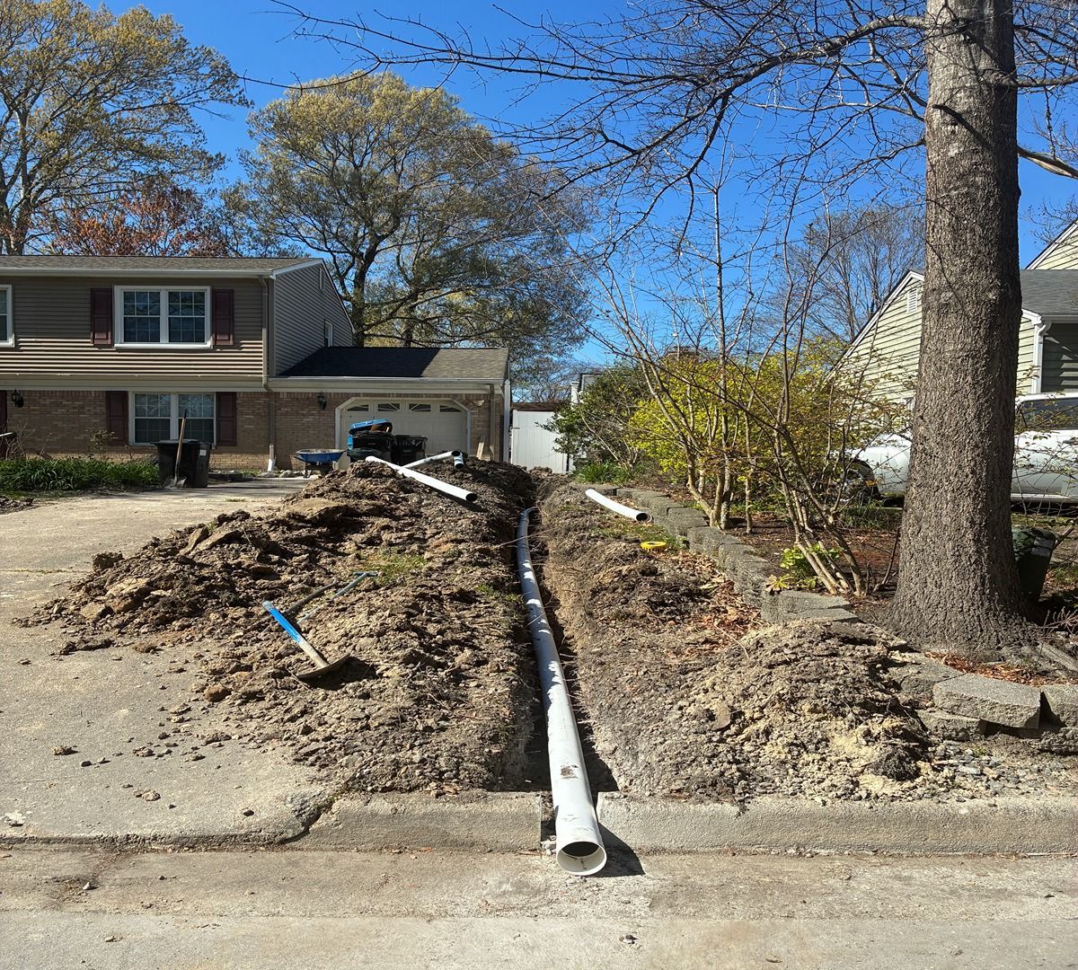 Front yard excavation with a large pipe trench leading to a suburban house under a clear blue sky