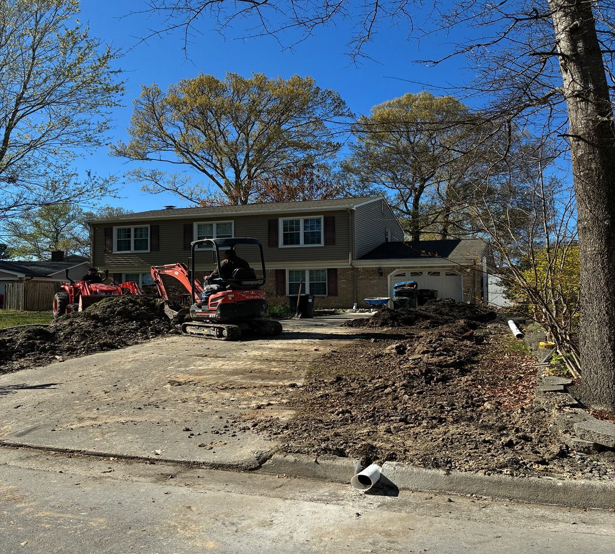 House with driveway debris and a tractor during yard cleanup under a blue sky