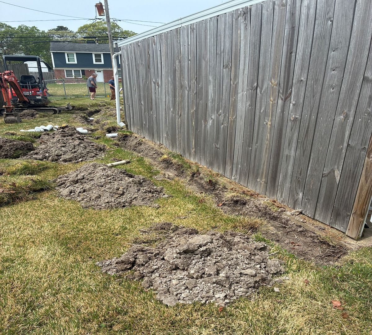 Backyard with dirt mounds beside a long wooden fence and a small excavator in the distance