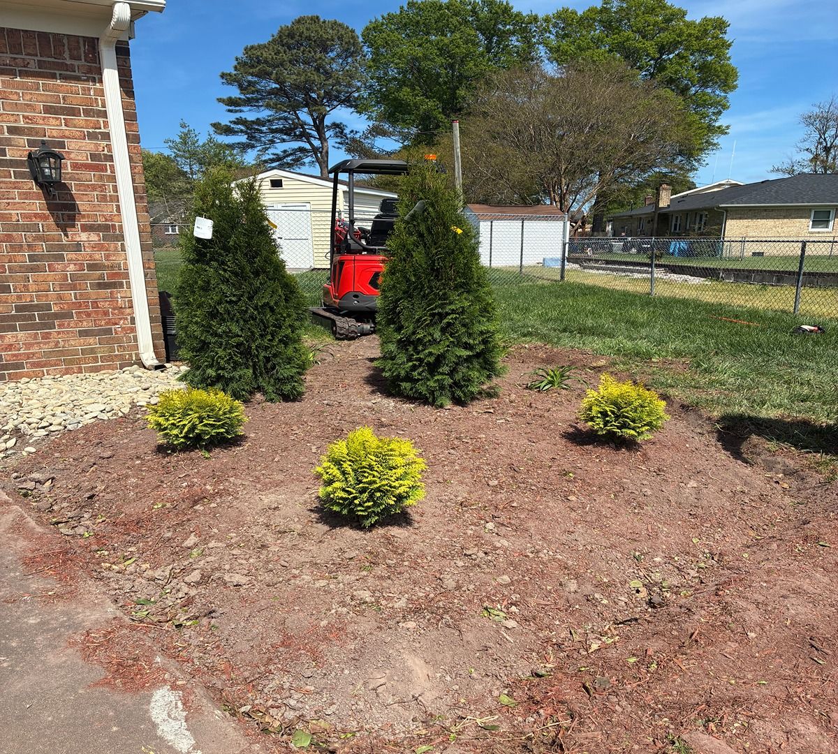 Front yard landscaping with small shrubs, mulch, and a red utility vehicle near a brick house