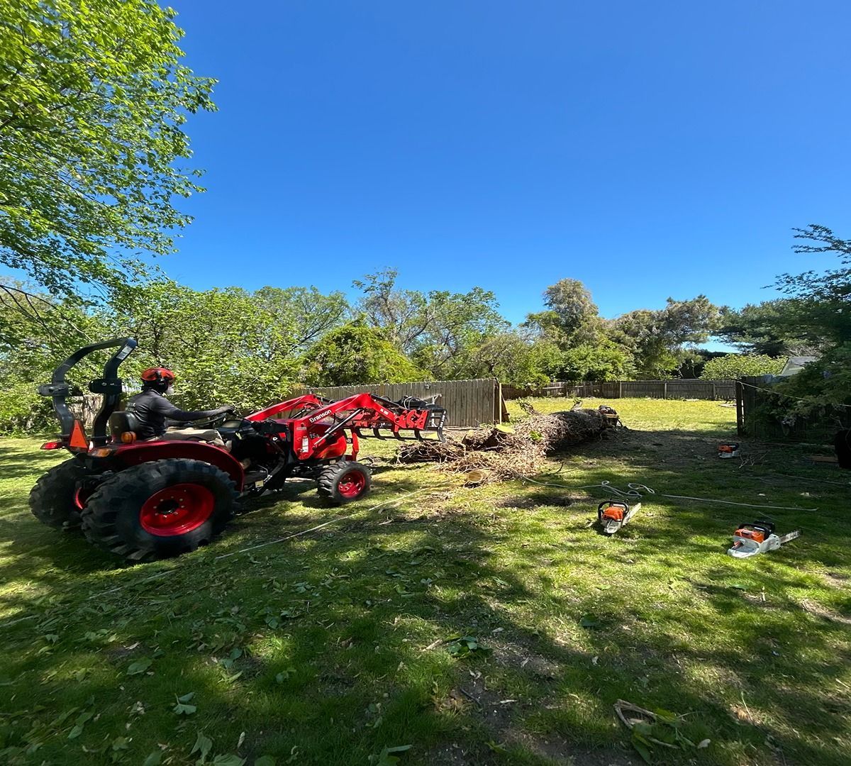 Person on a red tractor mowing a grassy yard under a bright blue sky.