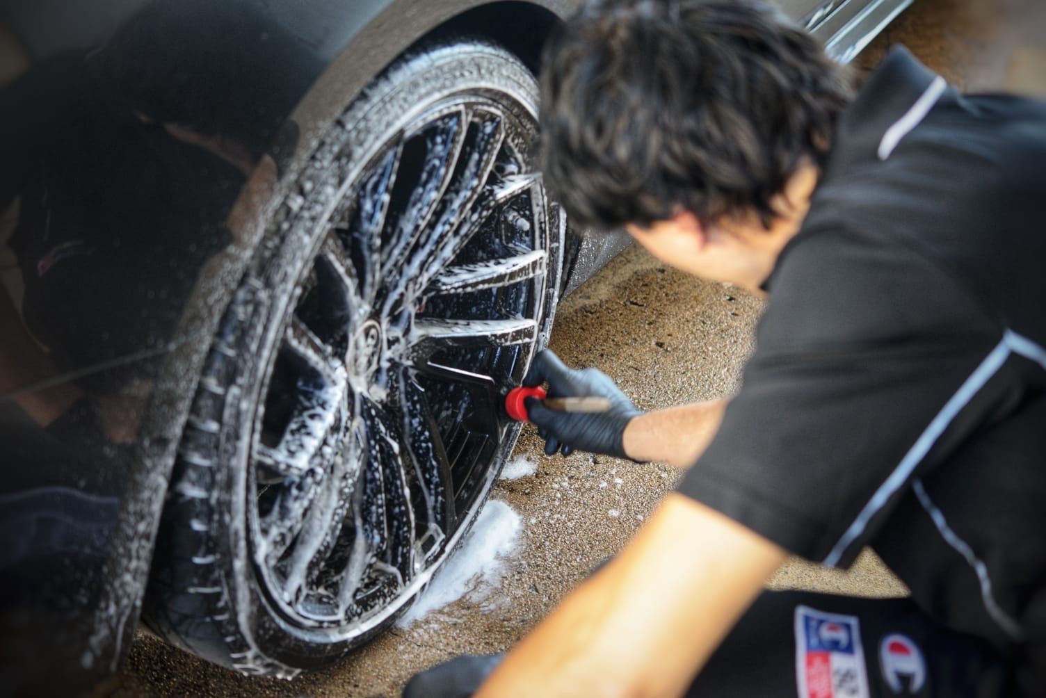 a Person is Cleaning the Rims of a Black Car With a Brush — Best Car Detailing in Vincent, QLD