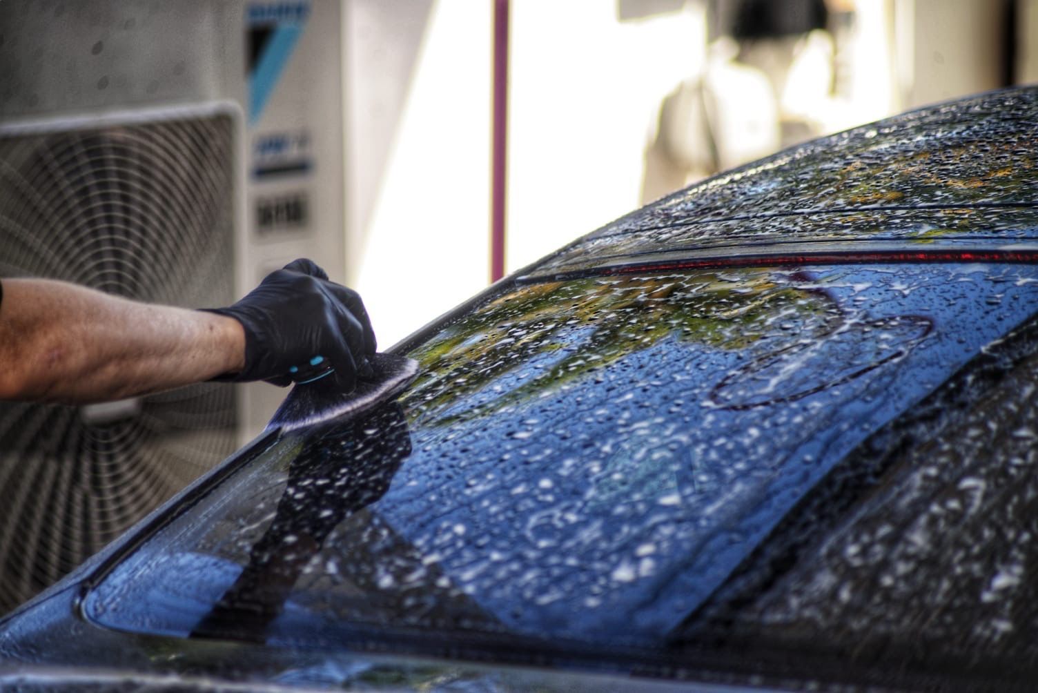 a Person is Washing the Front Windscreen of a Black Car — Best Car Detailing in Vincent, QLD