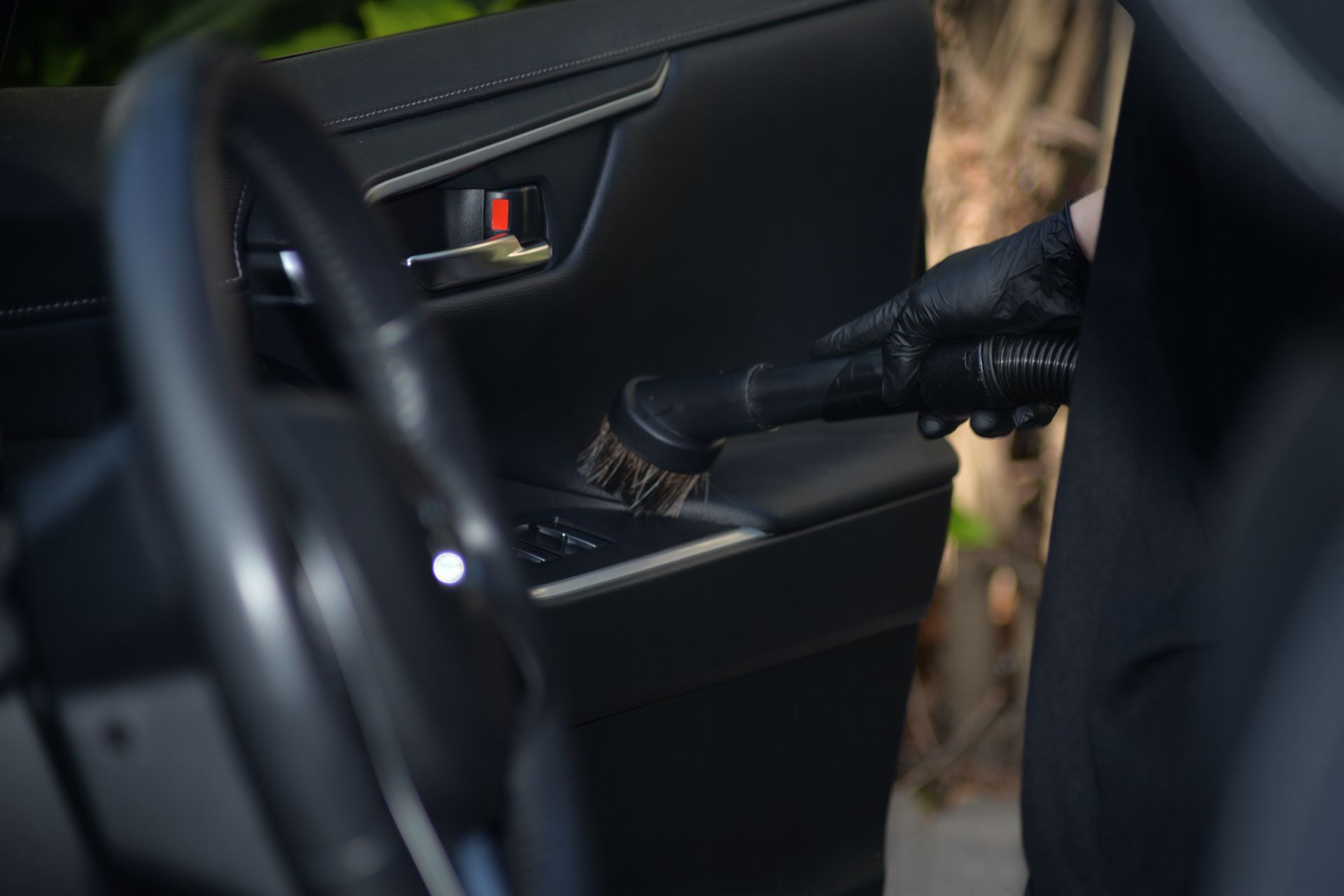 A Gloved Hand Vacuums a Car Door Panel With a Brush Attachment — Best Car Detailing in Vincent, QLD
