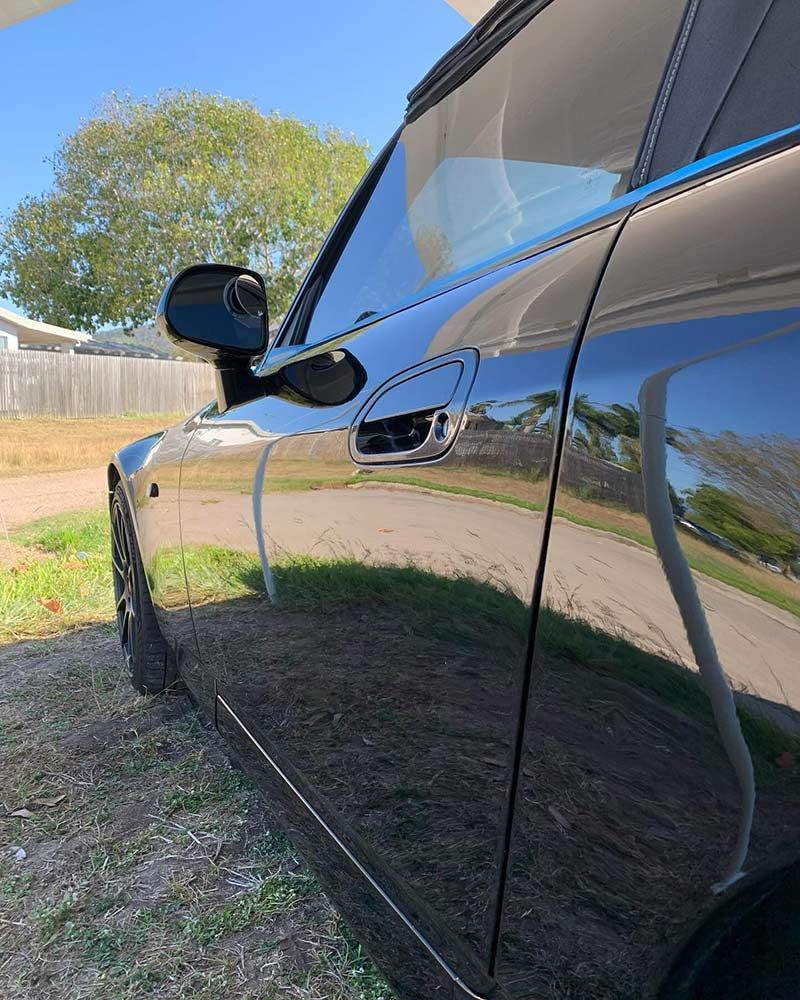 A Black Car is Parked in a Driveway Next to a Fence — Best Car Detailing in Vincent, QLD