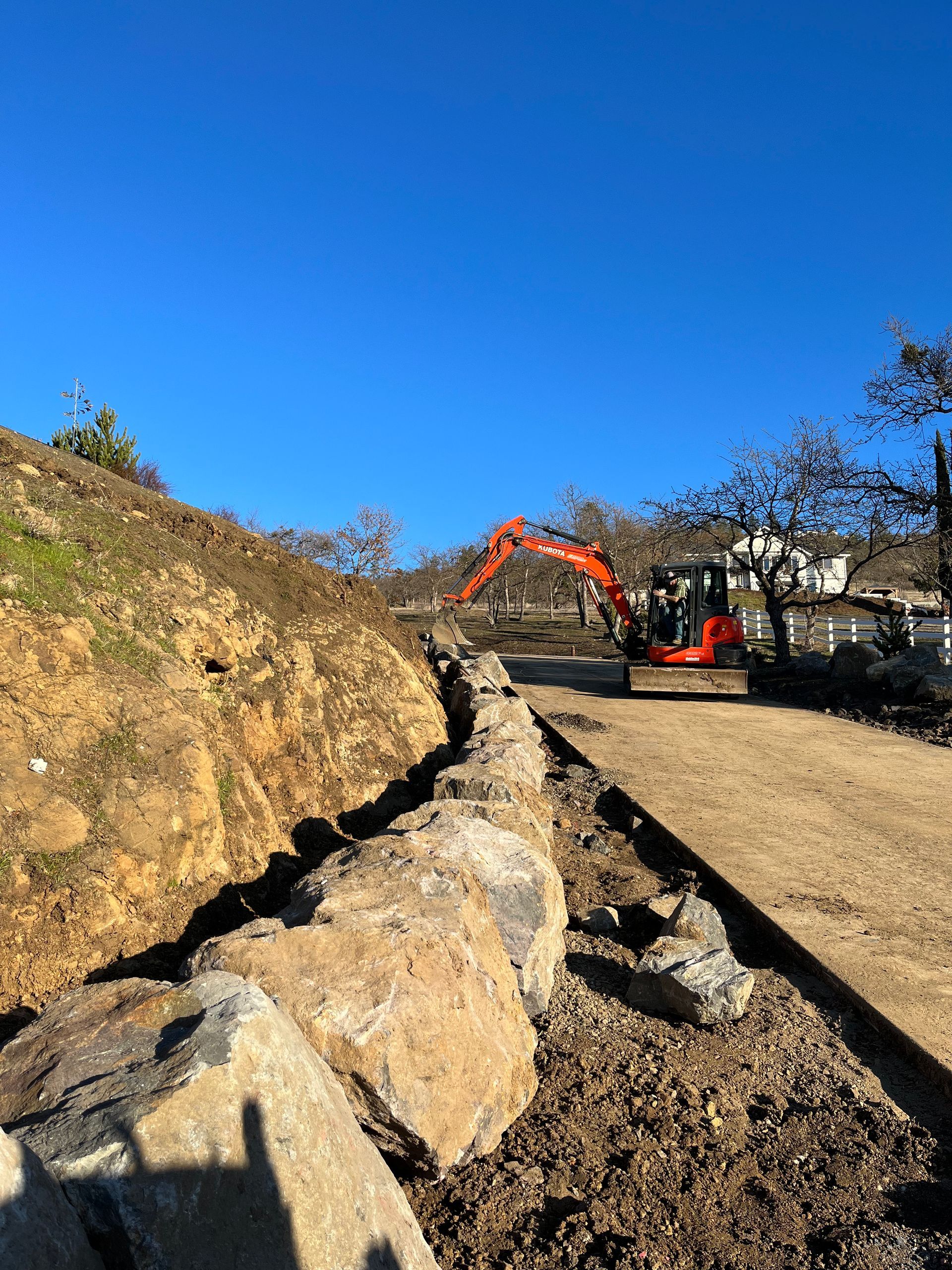 An excavator is working on a rock wall on a dirt road.