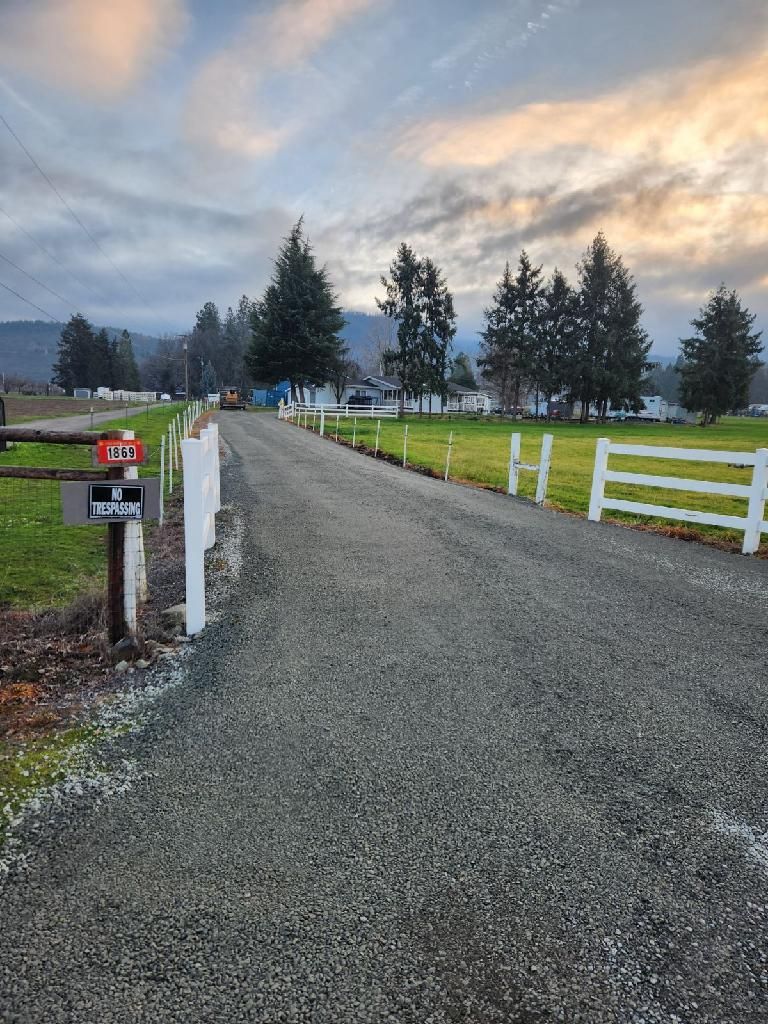 A gravel road with a white fence and a mailbox on the side of it.