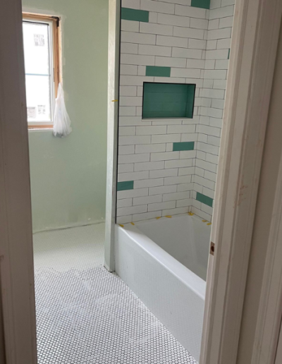 A bathroom with a tub and a shower with green tiles