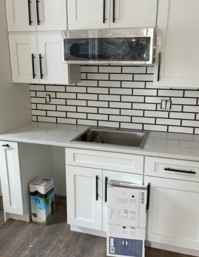 A kitchen with white cabinets , a sink , a microwave and a brick wall.