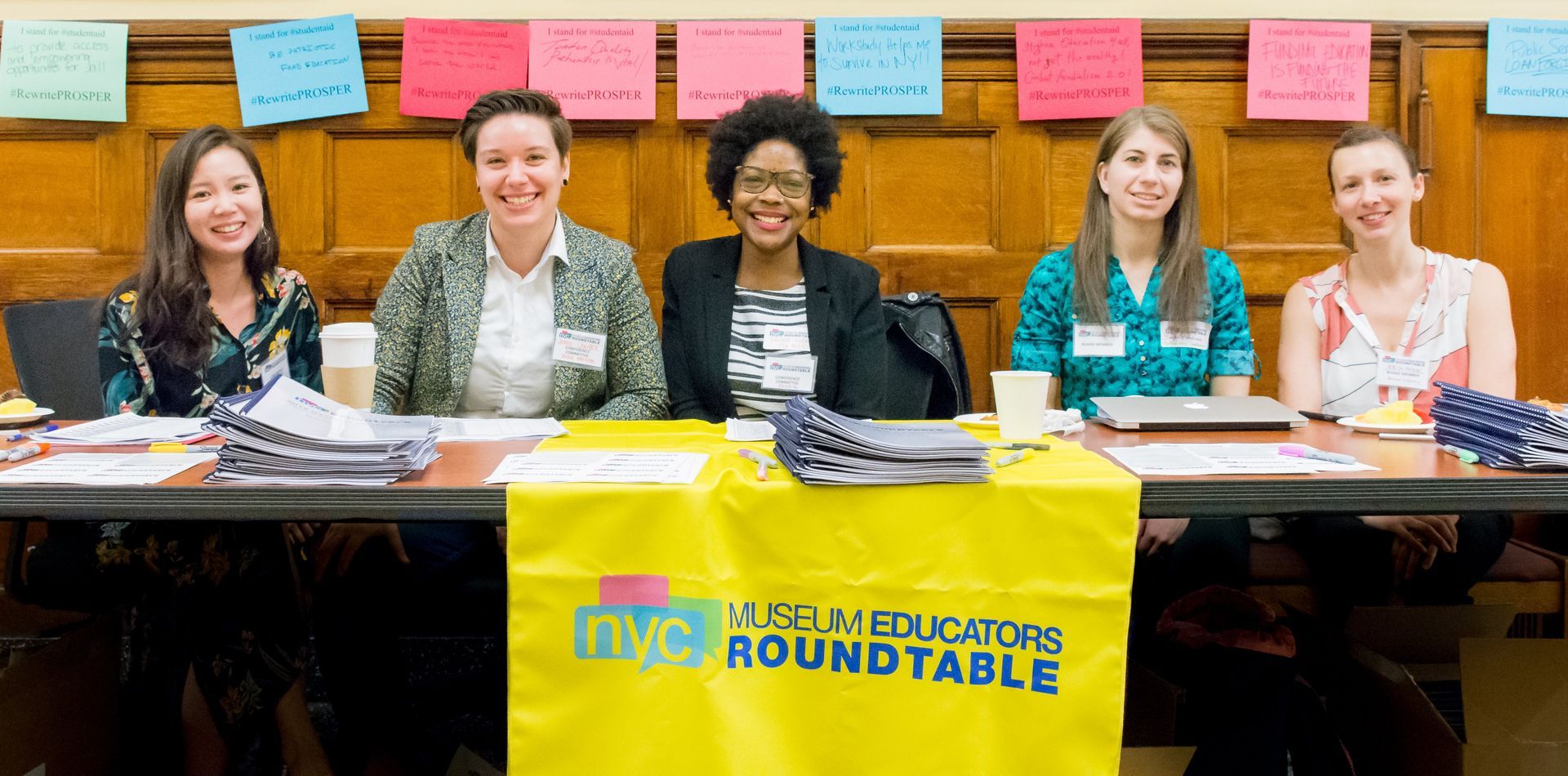 Five people sit behind a table with a yellow