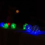 A string of decorative, spherical LED string lights glowing in blue, green, and red against a dark, out-of-focus background.