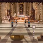 The interior of a cathedral featuring a long, tiled aisle leading to a lit altar with a large cross.