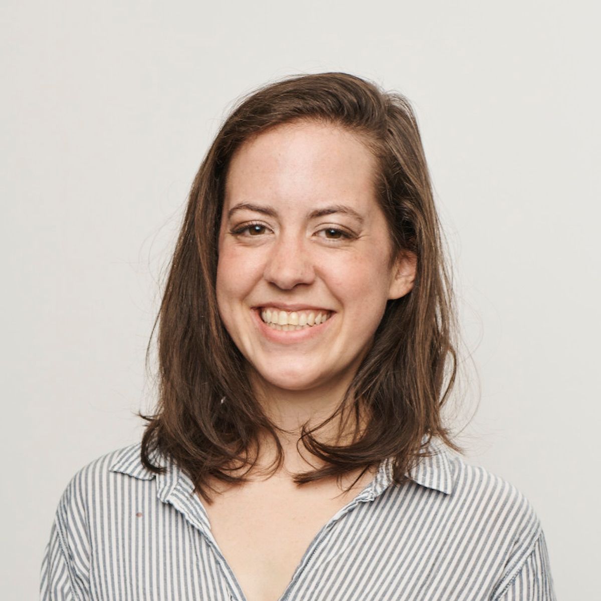 A person with dark, voluminous hair and eyes closed, smiling while touching their hair against a wooden panel background.