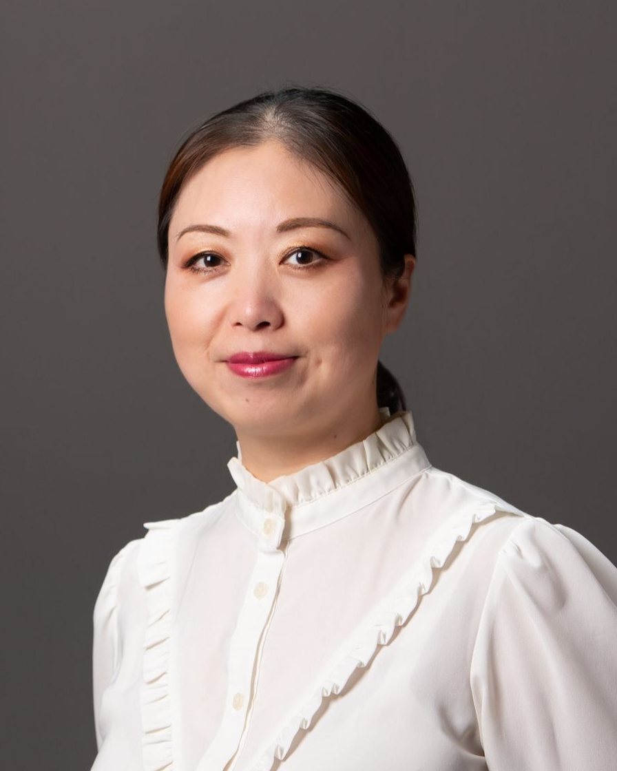 A person with dark, voluminous hair and eyes closed, smiling while touching their hair against a wooden panel background.